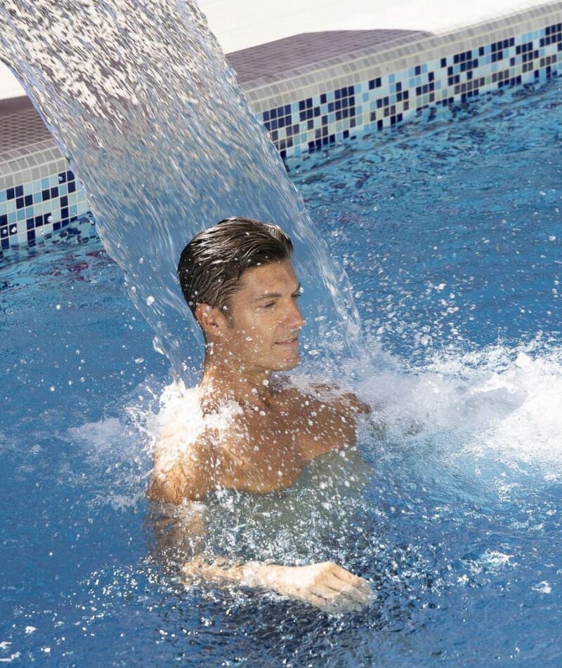 Uomo sotto cascata in piscina termale