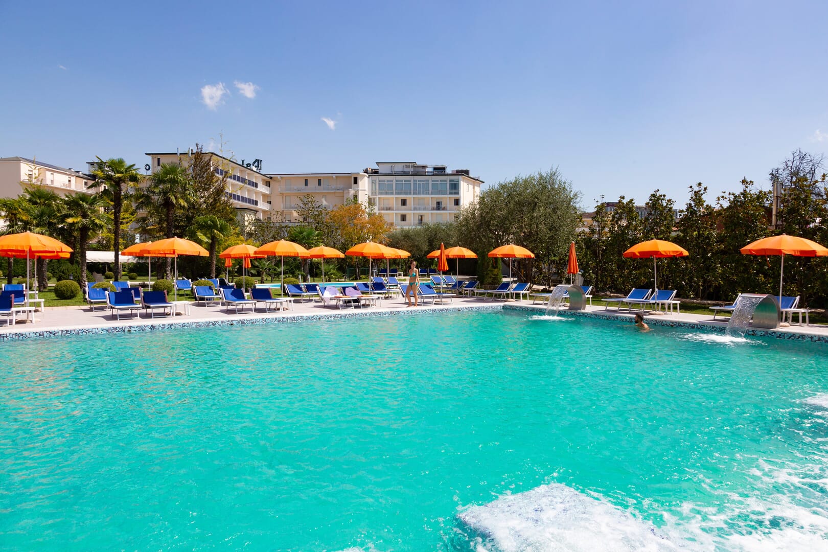 Piscina con ombrelloni arancioni e palme.