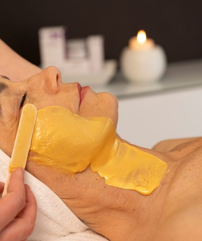 Donna riceve trattamento viso con maschera dorata.